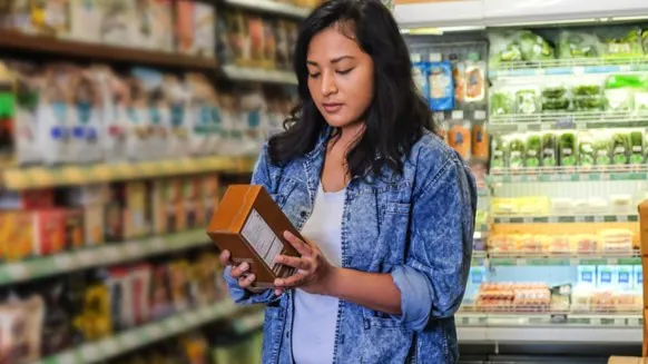 Women holding a packaged food box in a grocery store reading the nutrition facts or ingredient list - https://www.cdc.gov/salt/about/index.html