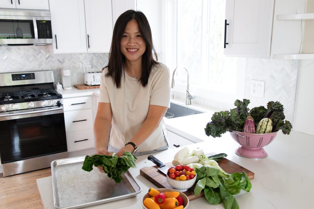 Smiling Asian woman preparing vegetables with a cutting board and roasting pan