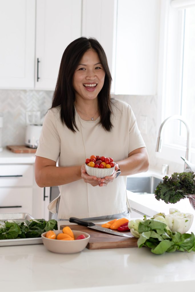 Smiling Asian woman with small bowl of vegetables in a modern kitchen