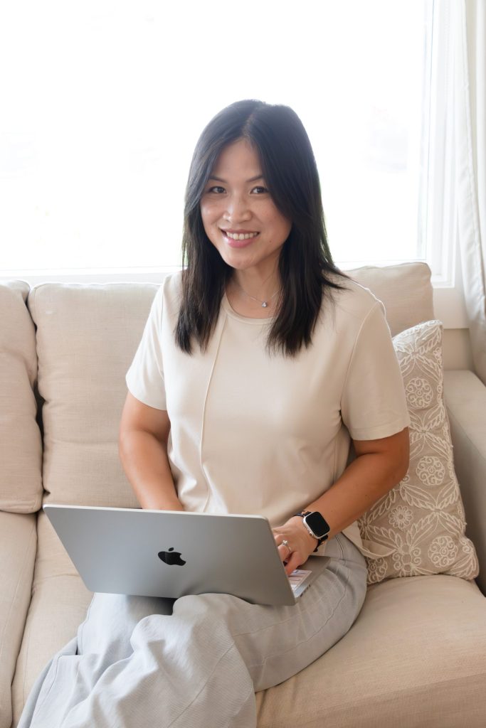 Smiling professional Asian woman sitting on couch and typing on a laptop