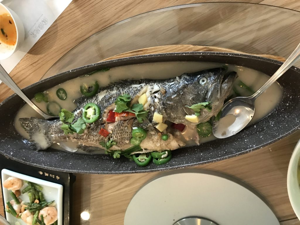 a whole fish in on a black plate with garnish of jalapenos, chili peppers, garlic, cilantro, and scallions.