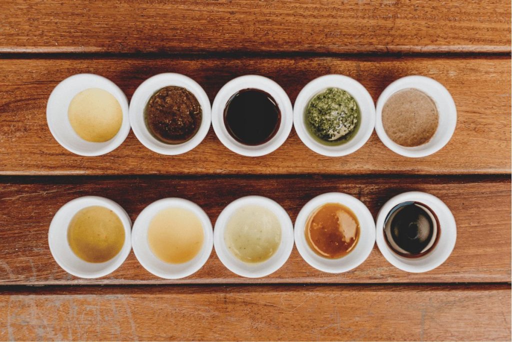 10 sauce dishes with a variety of different sauces -- lemon juice, chimmichuri, xo sauce, soy sauce, sesame sauce, vinegar, fish sauce, dumpling sauce, chili sauce